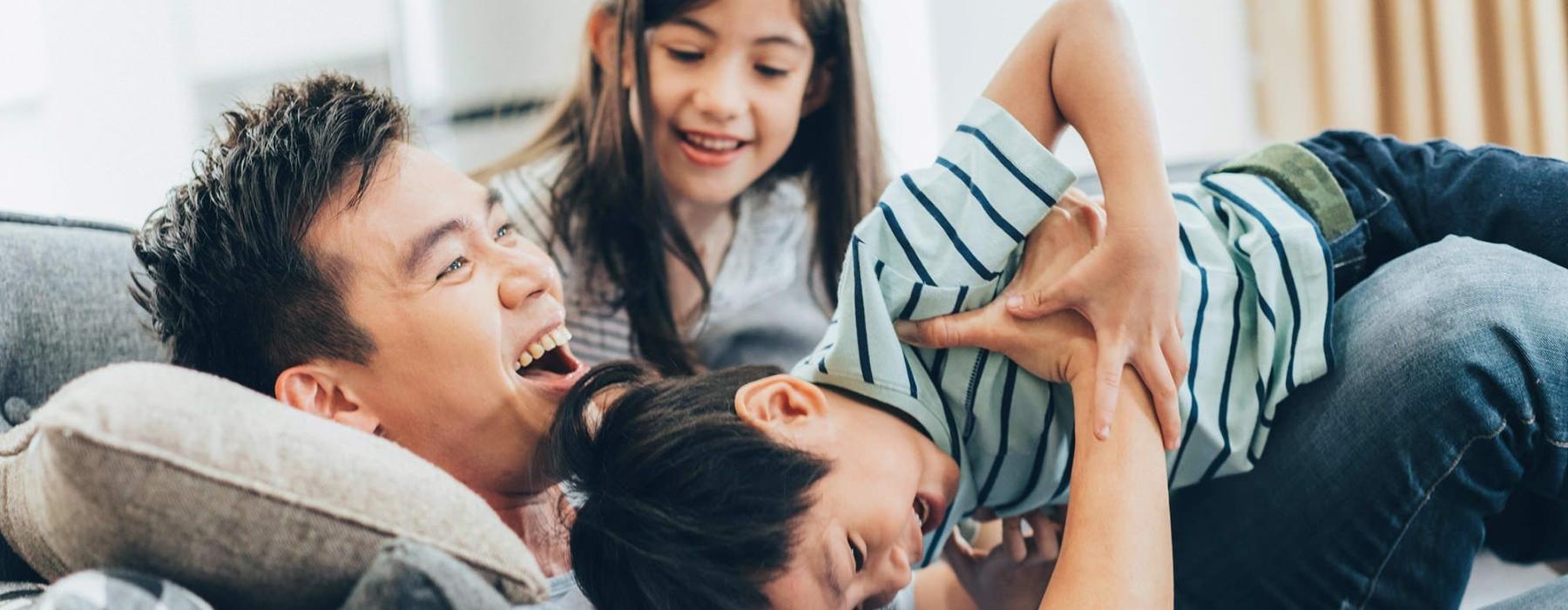 father plays on a couch with his young children