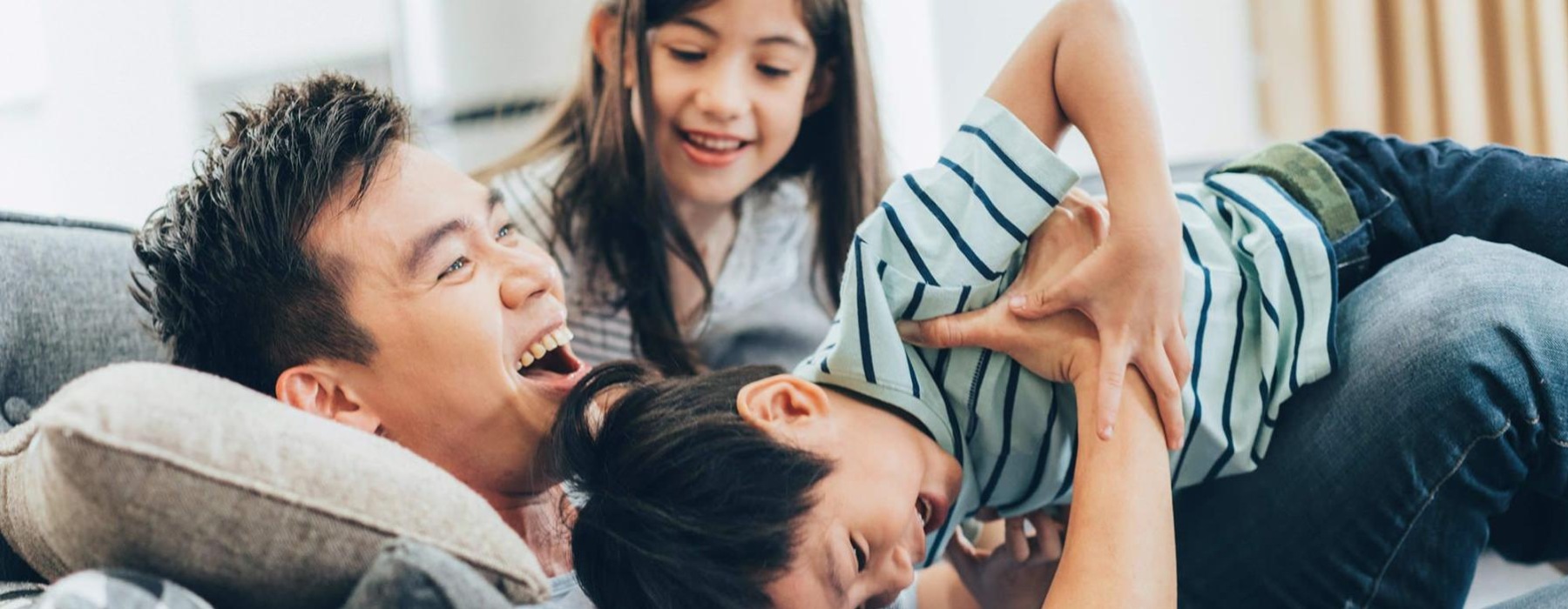 father plays on a couch with his young children